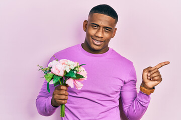 Young black man holding bouquet of white flowers smiling happy pointing with hand and finger to the side