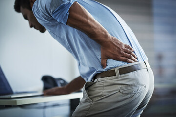 Its so painful I cant even stand up properly. Shot of a young businessman suffering with back pain at work. - obrazy, fototapety, plakaty