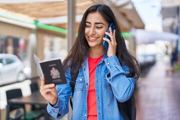 Young hispanic girl talking on the smartphone holding passport at street