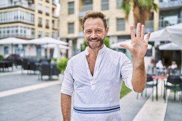 Middle age man outdoor at the city showing and pointing up with fingers number five while smiling...