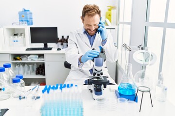 Fototapeta premium Middle age hispanic man wearing scientist uniform talking on the smartphone using microscope at laboratory