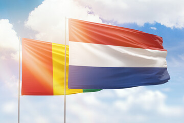 Sunny blue sky and flags of netherlands and guinea