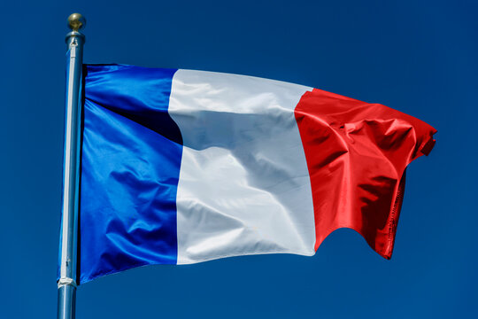 French flag on a metal flagpole against a blue cloudless sky as a symbol of France