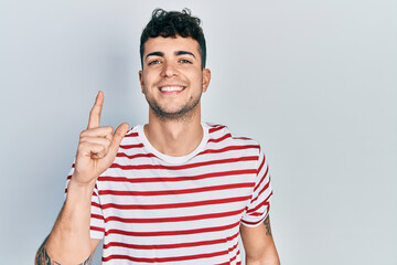 Young hispanic man wearing casual clothes smiling with an idea or question pointing finger up with happy face, number one