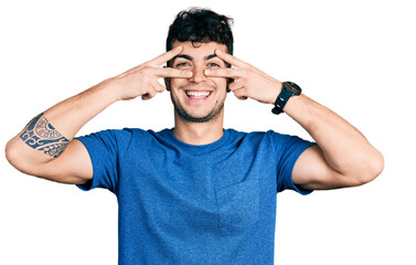 Young hispanic man wearing casual t shirt doing peace symbol with fingers over face, smiling cheerful showing victory