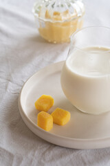 A glass of milk on a table with a white tablecloth. Glass jar with honey and yellow candies.