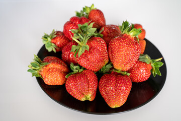 fresh ripe strawberries in a bowl black plate on a white table background