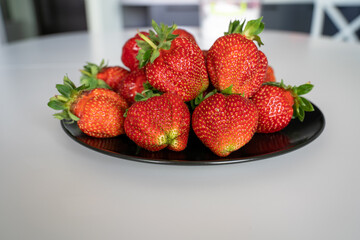 fresh ripe strawberries in a bowl black plate on a white table background