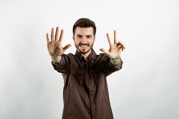 Happy young man wearing shirt posing isolated over white background showing and pointing up with fingers number eight while smiling.