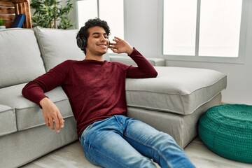 Young hispanic man listening to music sitting on the floor at home.