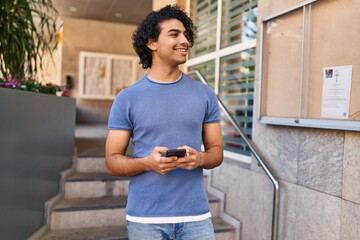 Fototapeta premium Young hispanic man smiling confident using smartphone at street
