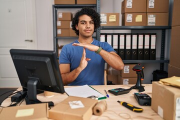Fototapeta premium Hispanic man with curly hair working at small business ecommerce doing time out gesture with hands, frustrated and serious face