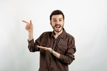 Fototapeta premium Cheerful young man wearing brown shirt posing isolated over white background smiling while pointing with finger to his empty open hand palm.