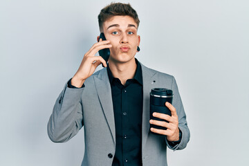 Young caucasian boy with ears dilation using smartphone and drinking a cup of coffee looking at the camera blowing a kiss being lovely and sexy. love expression.