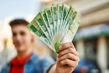 Young caucasian guy smiling holding russian ruble banknotes at the city