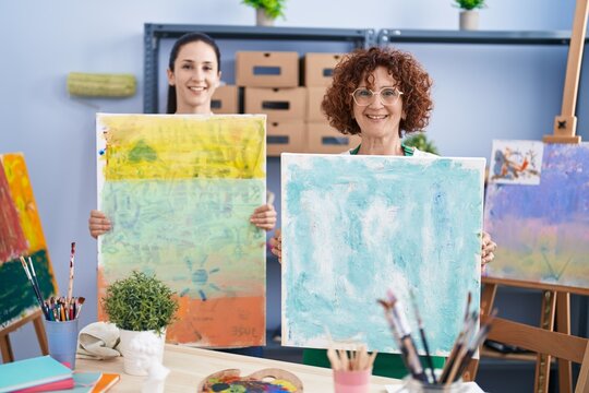 Two women artists smiling confident holding canvas draw at art studio