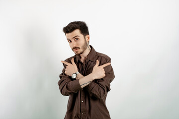 Caucasian man wearing brown shirt posing isolated over white background crossed hands and pointing to copy space on both sides.