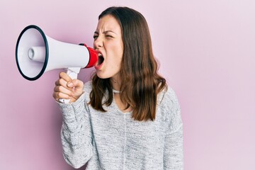 Young brunette woman shouting and screaming through megaphone over pink isolated background