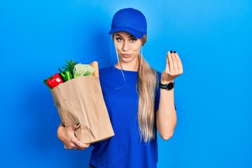 Young caucasian woman wearing courier uniform with groceries from supermarket doing italian gesture...