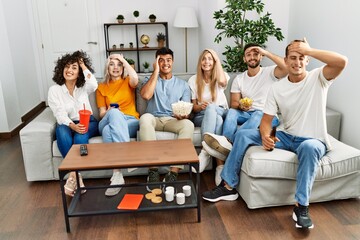 Group of people eating snack sitting on the sofa at home stressed and frustrated with hand on head, surprised and angry face