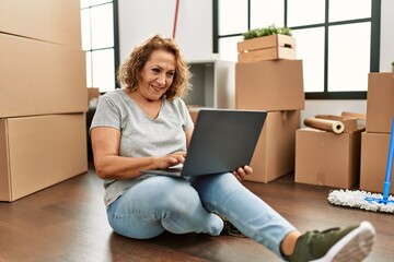 Middle age caucasian woman using laptop sitting on the floor at new home.