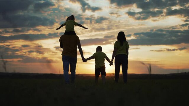 Happy family. Children with parents in park on grass. Family fun at sunset. Silhouette people are walk in park.Summer walk in park. Child holds hand of parents.Happy family concept.Free family in park