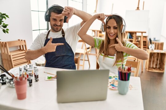 Young couple of wife and husband at art studio looking at video on laptop smiling making frame with hands and fingers with happy face. creativity and photography concept.
