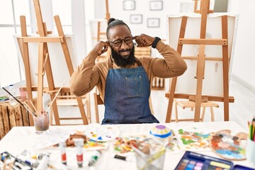 African american artist man at art studio covering ears with fingers with annoyed expression for the noise of loud music. deaf concept.