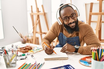 Young african american artist man using headphones drawing at art studio.