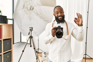 African american photographer man working at photography studio smiling positive doing ok sign with hand and fingers. successful expression.