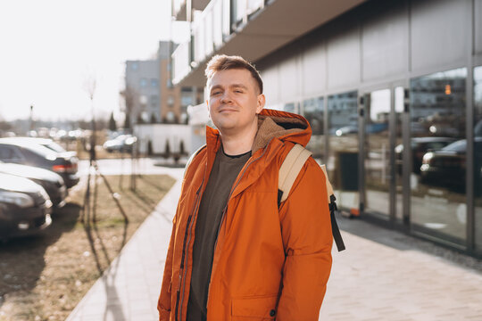 A handsome young man with backpack walking on the street in the city. Urban lifestyle concept. Traveler. Spring time. Portrait of happy young man in casual clothing looking at camera outdoor.