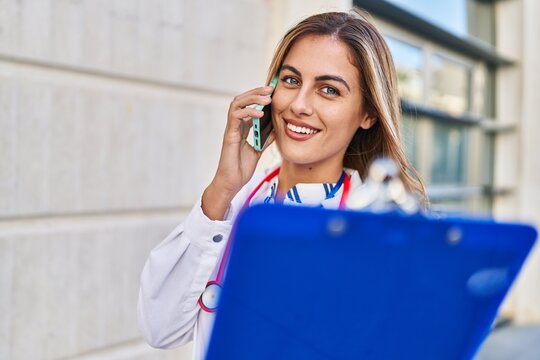 Young blonde woman wearing doctor uniform talking on the smartphone at hospital