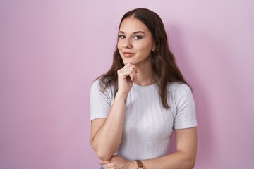 Young hispanic girl standing over pink background with hand on chin thinking about question, pensive expression. smiling and thoughtful face. doubt concept.