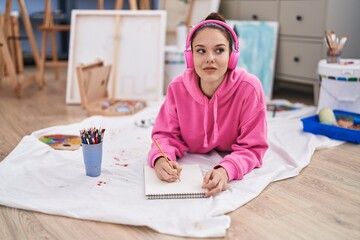 Young woman artist listening to music drawing on notebook at art studio