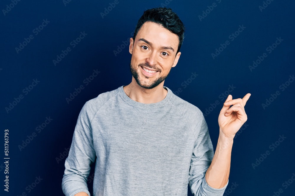 Canvas Prints Young hispanic man wearing casual clothes with a big smile on face, pointing with hand and finger to the side looking at the camera.