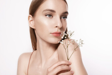 Portrait of a beautiful young woman with glowing clear skin on a white background with a white flower. A girl with natural beauty and a pretty face