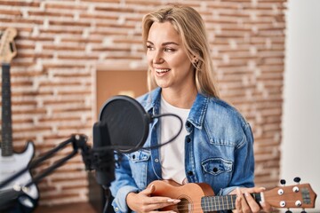 Fototapeta na wymiar Young blonde woman musician singing song playing ukelele at music studio