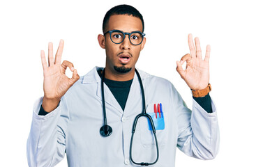 Fototapeta premium Young african american man wearing doctor uniform and stethoscope looking surprised and shocked doing ok approval symbol with fingers. crazy expression