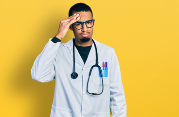 Young african american man wearing doctor uniform and stethoscope worried and stressed about a problem with hand on forehead, nervous and anxious for crisis