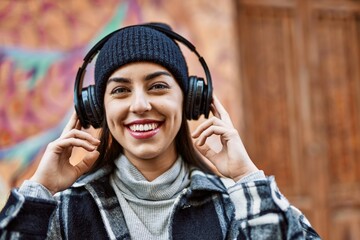 Young hispanic woman smiling happy using headphones at the city.