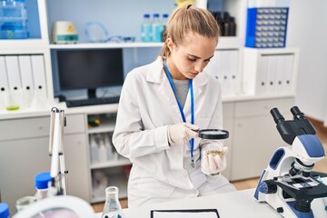 Fototapeta na wymiar Young blonde woman wearing scientist uniform using loupe at laboratory