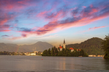 Church of the Assumption of the Blessed Virgin Mary on an island on Lake Bled in Slovenia. There is a dramatic sky in the sky with a colorful rainbow.