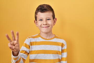 Young caucasian kid standing over yellow background showing and pointing up with fingers number three while smiling confident and happy.