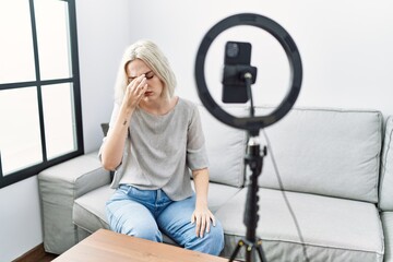 Fototapeta na wymiar Young caucasian woman recording vlog tutorial with smartphone at home tired rubbing nose and eyes feeling fatigue and headache. stress and frustration concept.