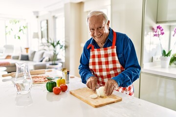 Senior man smiling confident cutting onion at kitchen