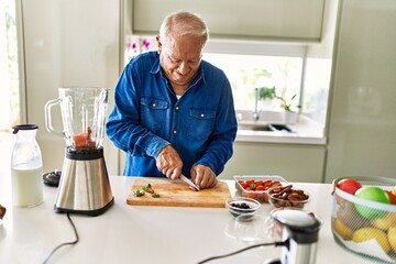 Senior man smiling confident cutting datil at kitchen