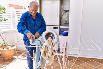 Senior caucasian man smiling happy putting clothes on clothesline at the terrace.
