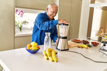 Senior man smiling confident shaking blender at kitchen