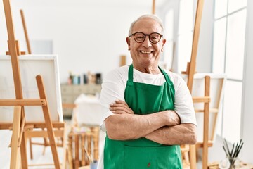 Senior grey-haired artist man smiling happy standing with arms crossed gesture at art studio.