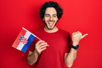 Handsome hispanic man holding croatia flag pointing thumb up to the side smiling happy with open mouth - obrazy, fototapety, plakaty